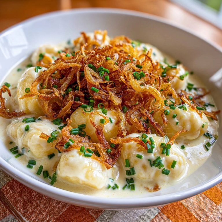 Cremige Kartoffelgnocchi mit Röstzwiebeln, serviert in einer weißen Schüssel, garniert mit frischen Kräutern und knusprigen Zwiebeln.