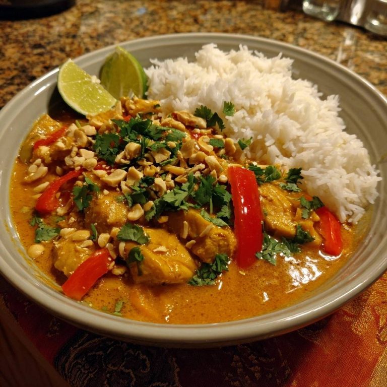 Cremiges Thai-Erdnuss-Hühnercurry serviert in einer Schüssel, garniert mit Erdnüssen, Koriander und einer Limettenspalte, serviert mit Reis.