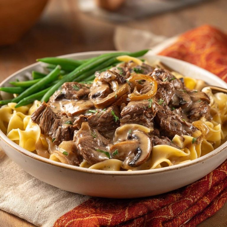 Saftiges Rindergeschnetzeltes mit Pilzen in Sahnesoße zu Bandnudeln, nahaufnahme des cremigen Gerichts mit grünen Bohnen