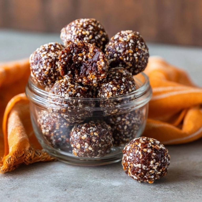 Sesam-Dattel-Energy-Balls mit Sesam ummantelt, einer aufgeschnitten, um die dunkle Dattel-Füllung zu zeigen. Köstliche, gesunde Energie-Happen in einem Glas.