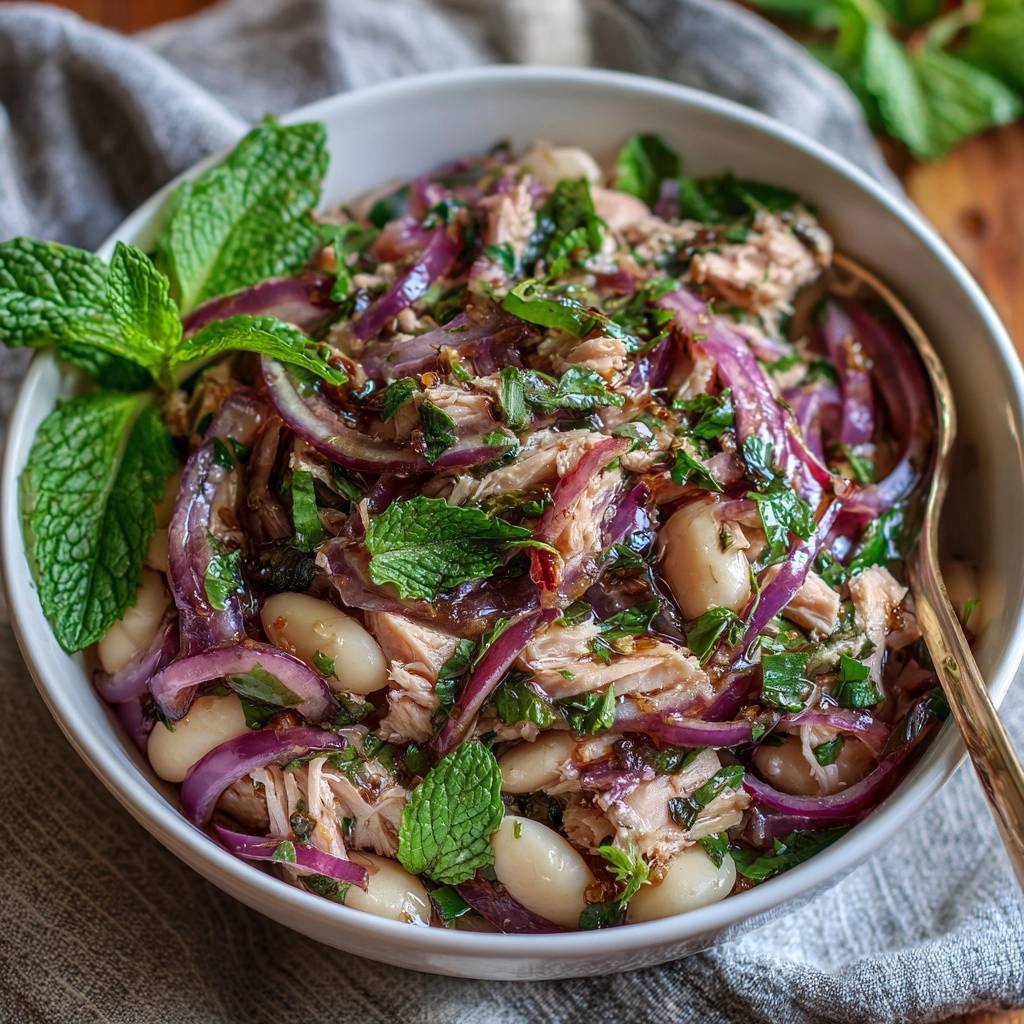 Frischer Bohnensalat mit Thunfisch, Minze und roten Zwiebeln, serviert in einer weißen Schüssel, von oben betrachtet, mit frischer Minze garniert.