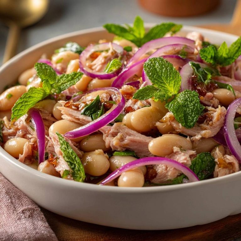 Frischer Bohnensalat mit Thunfisch, Minze und roten Zwiebeln in Nahaufnahme, garniert mit frischer Minze und roten Zwiebelringen, serviert in einer weißen Schüssel.