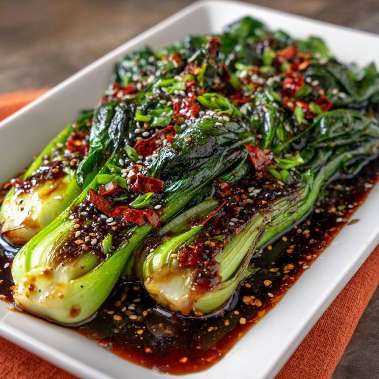 Knackiger Bok Choy mit Chili-Sesam-Soße serviert in einer weißen Platte, garniert mit Chili-Flocken und Sesamkörnern.