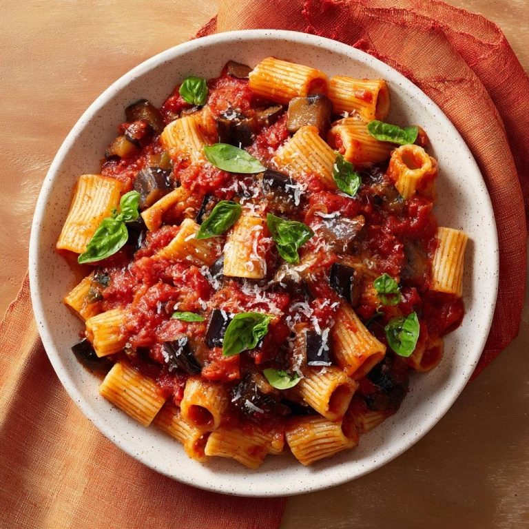 Rigatoni mit Auberginen-Tomaten-Sauce, serviert in einer Schüssel, garniert mit frischem Basilikum und Parmesan, präsentiert in einer Draufsicht.