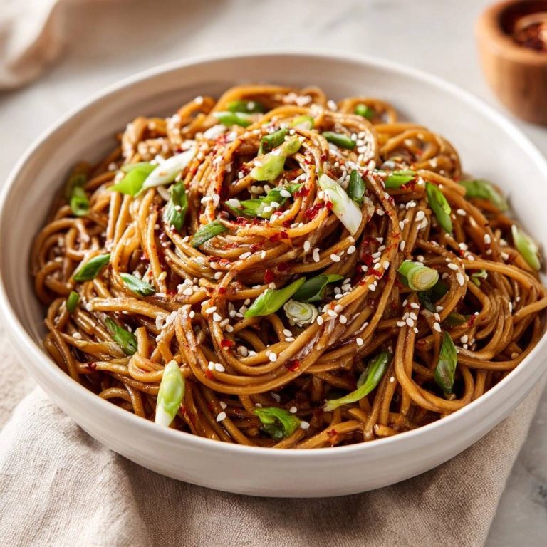 Scharfe Sesam-Chili-Nudeln in einer Schüssel serviert, garniert mit Sesam, Chili-Flocken und frischen Frühlingszwiebeln.