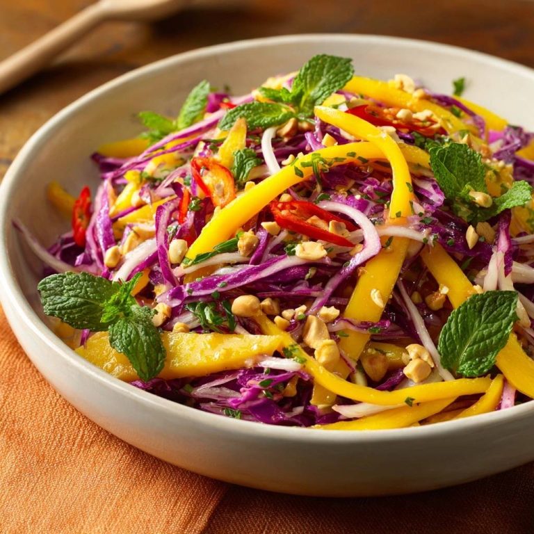 Thailändischer Mango-Rotkohl-Salat, serviert in einer Schüssel, garniert mit frischer Minze, Erdnüssen und Chili, in Nahaufnahme von oben.