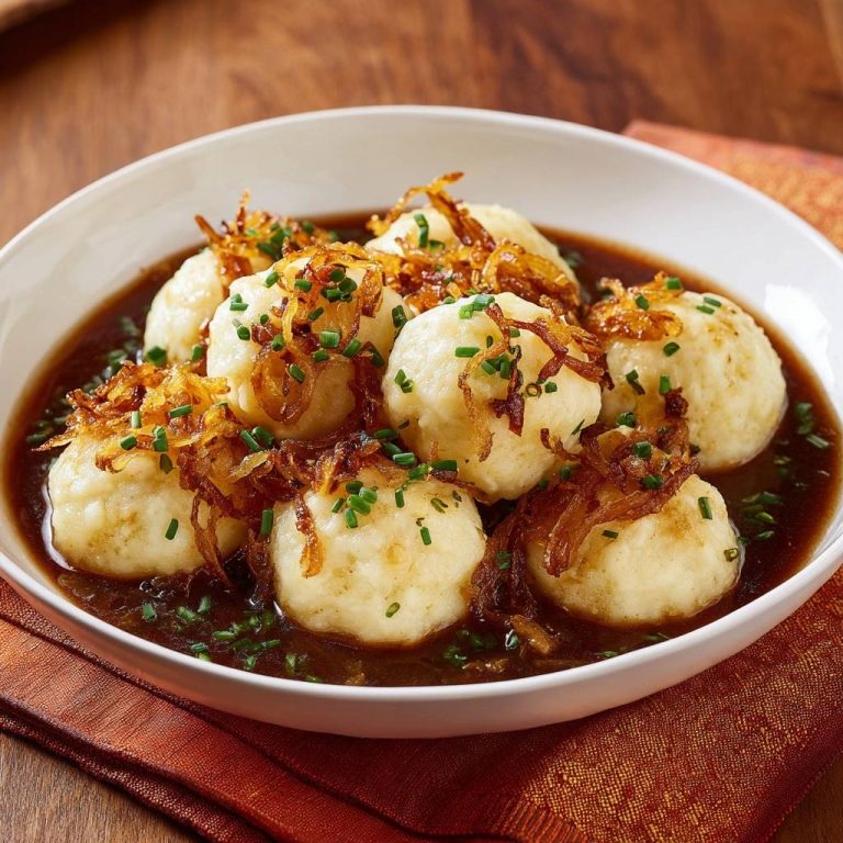 Fluffige Kartoffelknödel in würziger Zwiebelsoße, serviert in einer weißen Schüssel und garniert mit gebratenen Zwiebeln und Schnittlauch.