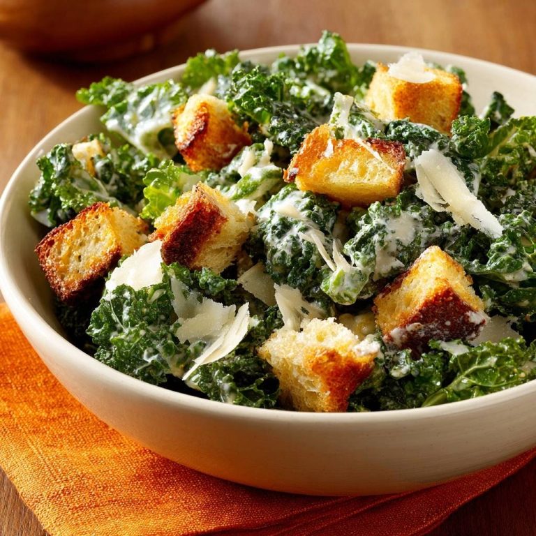 Cremiger Kale-Caesar-Salat, serviert in einer cremefarbenen Schüssel, zeigt eine Nahaufnahme der frischen Zutaten, einschließlich knuspriger Croûtons und Parmesan.
