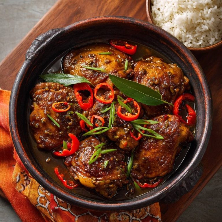Glasiertes Chili-Hähnchen mit roten Chilis und Frühlingszwiebeln, garniert mit frischen Kräutern, serviert in einer Tonschüssel.