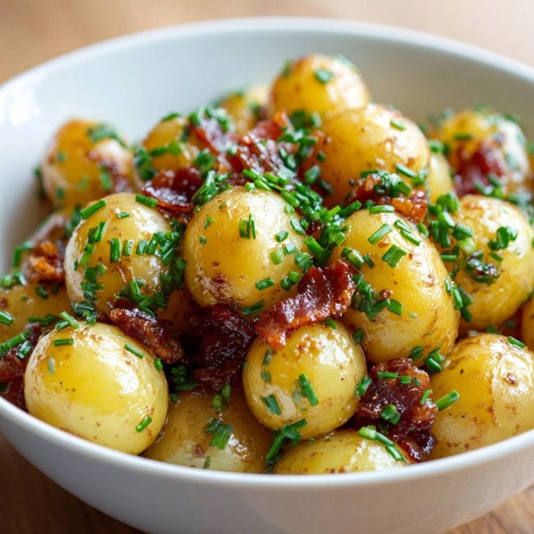 Goldene Babykartoffeln mit Speck und Schnittlauch in einer weißen Schüssel, von oben aufgenommen, reichlich garniert mit frischem Schnittlauch.